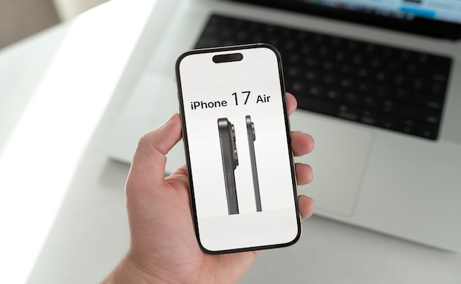 Mano sosteniendo un iPhone 17 Air frente a laptop