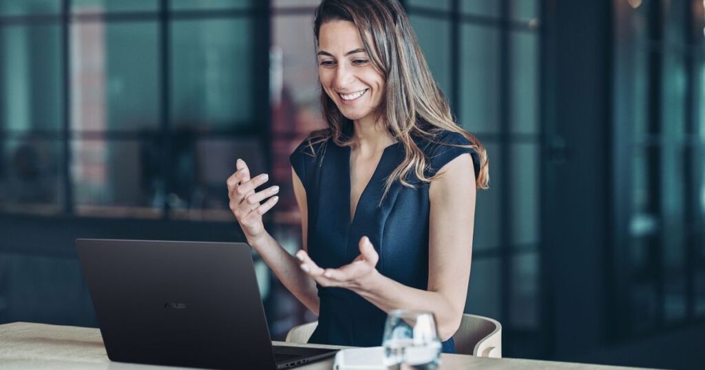 Mujer sonriendo mientras usa un laptop ASUS ExpertBook B3 G2 en una oficina moderna