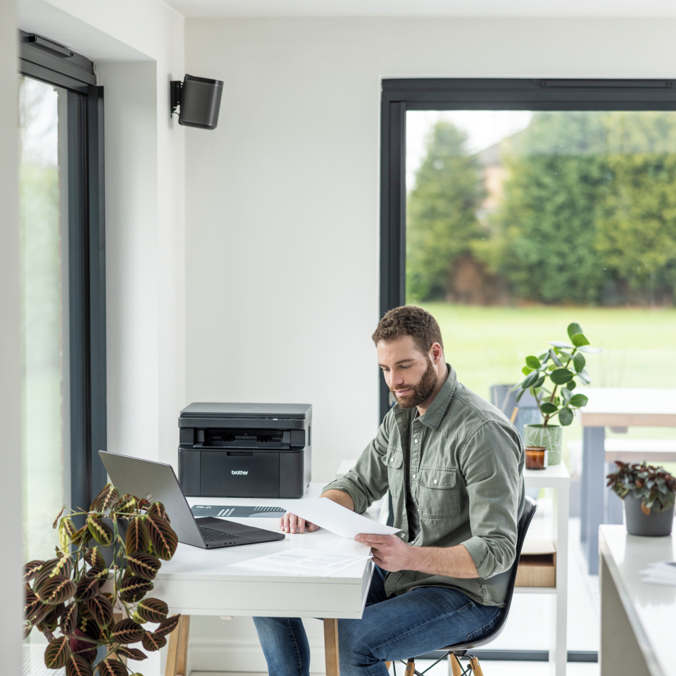 Hombre revisando documentos junto a impresora Brother en oficina moderna.