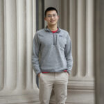 Estudiante de MIT, Alex Tang, posando entre columnas arquitectónicas.