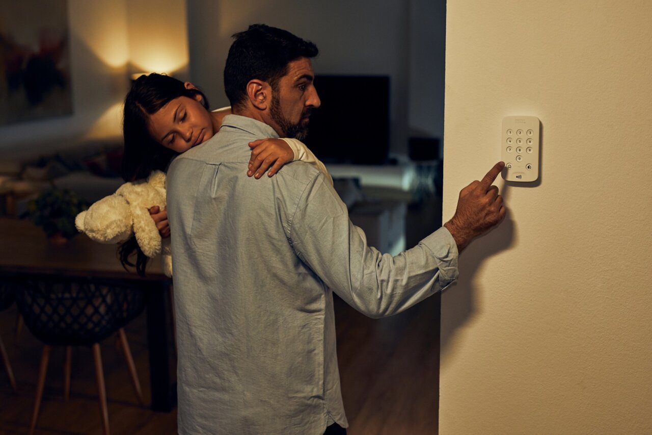 Padre con su hija en brazos activando alarma en casa